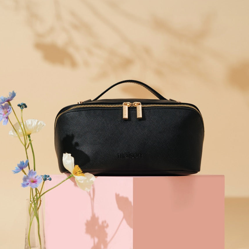 Black cosmetic bag with gold accents on a beige background